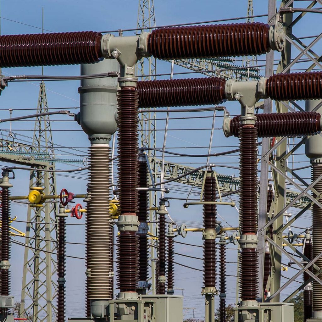 Close-up of brown ceramic high-voltage insulators and electrical switchyard components at an electricity transmission substation.