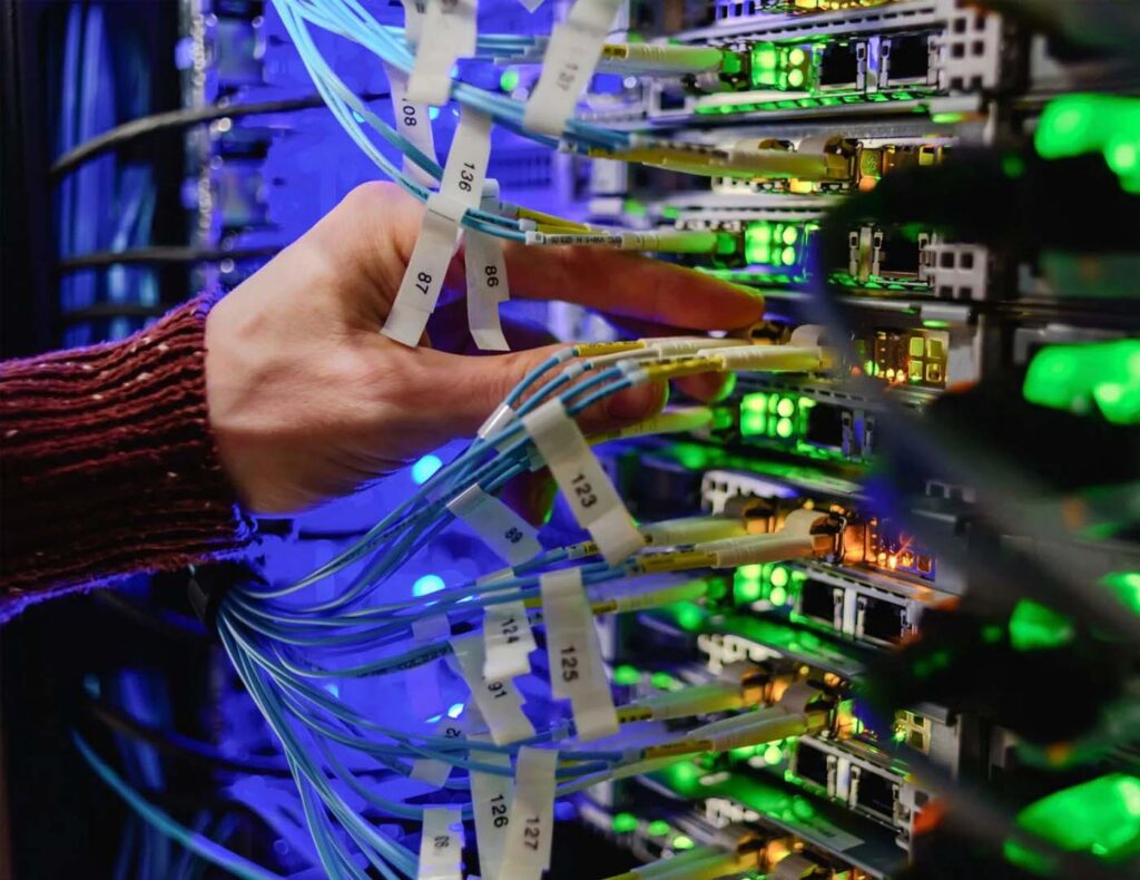 A network technician's hand organizing labeled fiber optic cables connected to a high-speed server switch in a data center.
