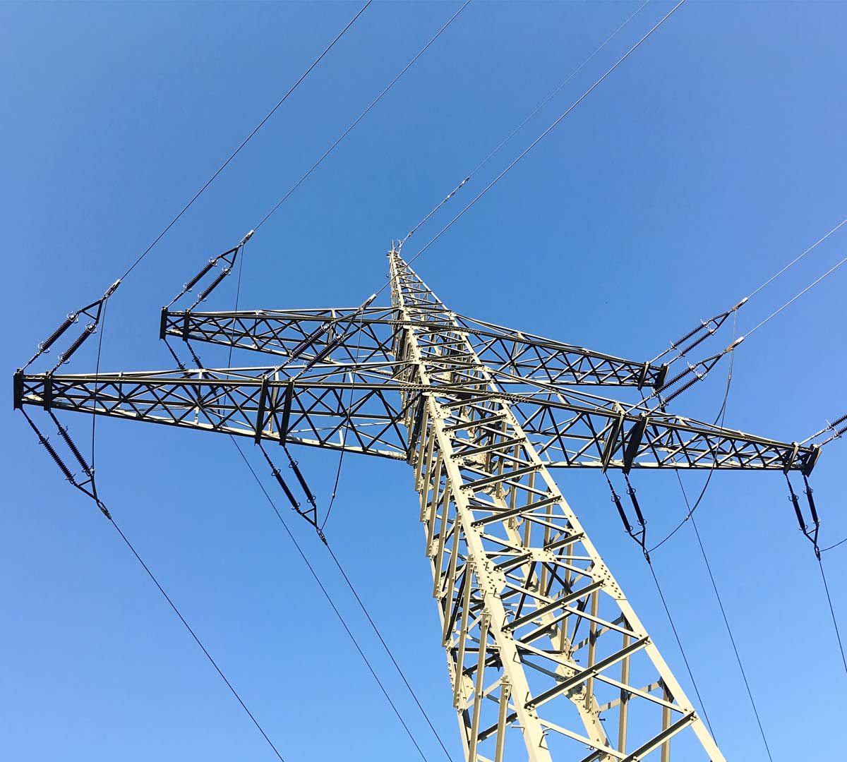 High-voltage steel lattice transmission tower supporting overhead power lines against a cloudy sky.