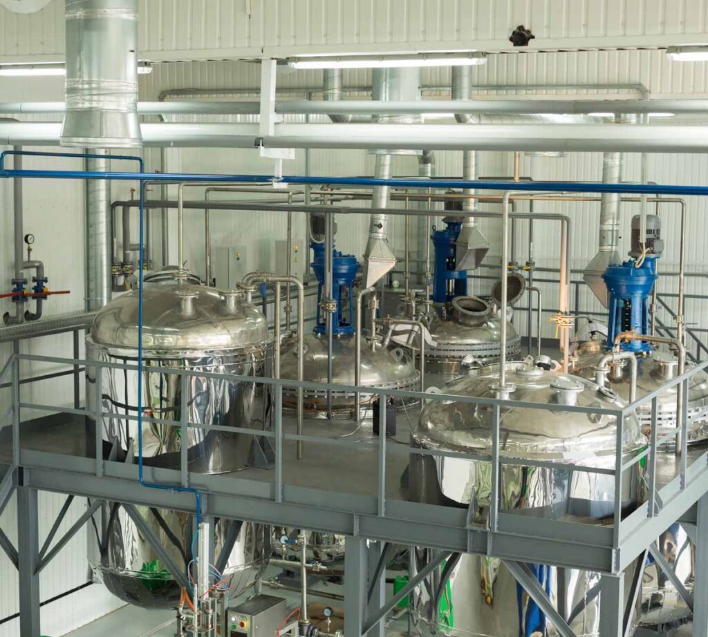 Stainless steel industrial processing tanks and mixing equipment in a clean manufacturing production facility.