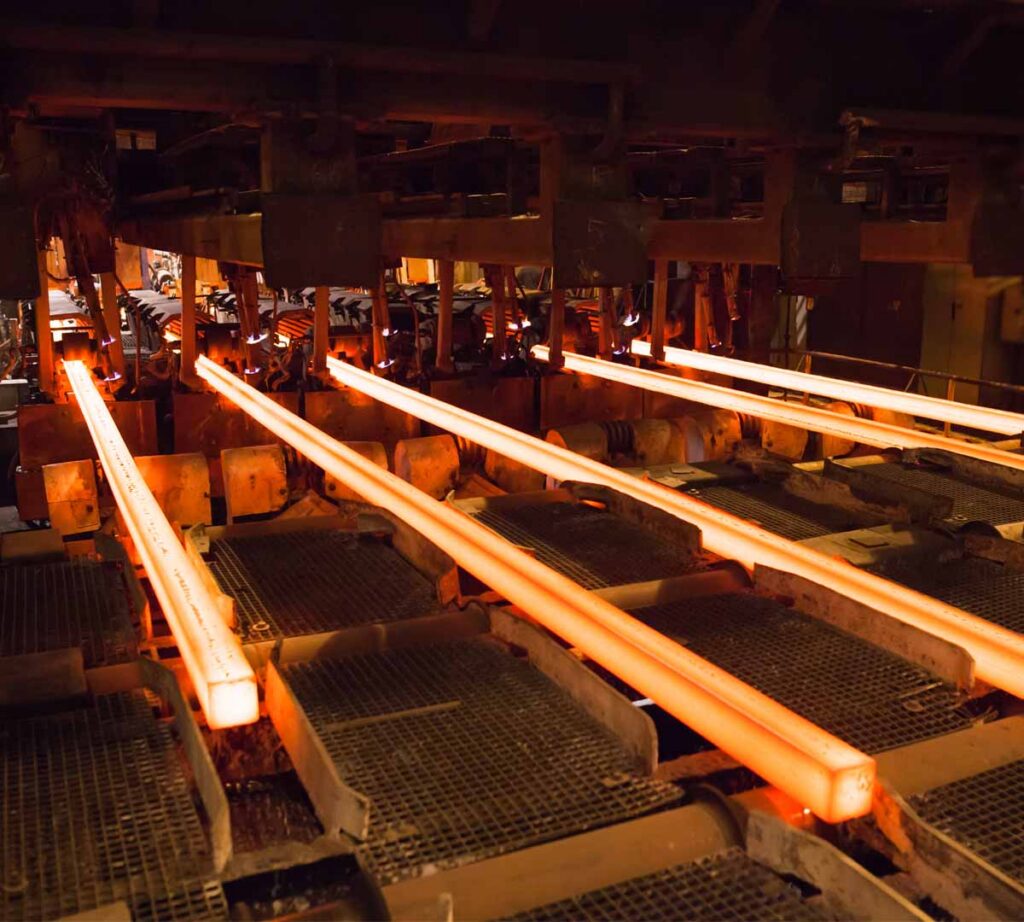 Industrial hot rolling mill production line processing glowing steel billets in a heavy manufacturing plant.