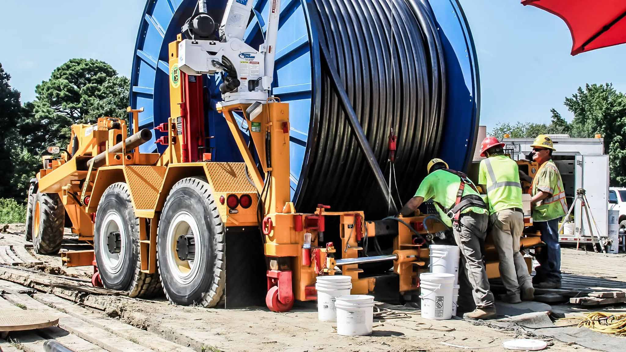 A field construction crew operating a heavy-duty cable reel trailer to install large subterranean utility cables.